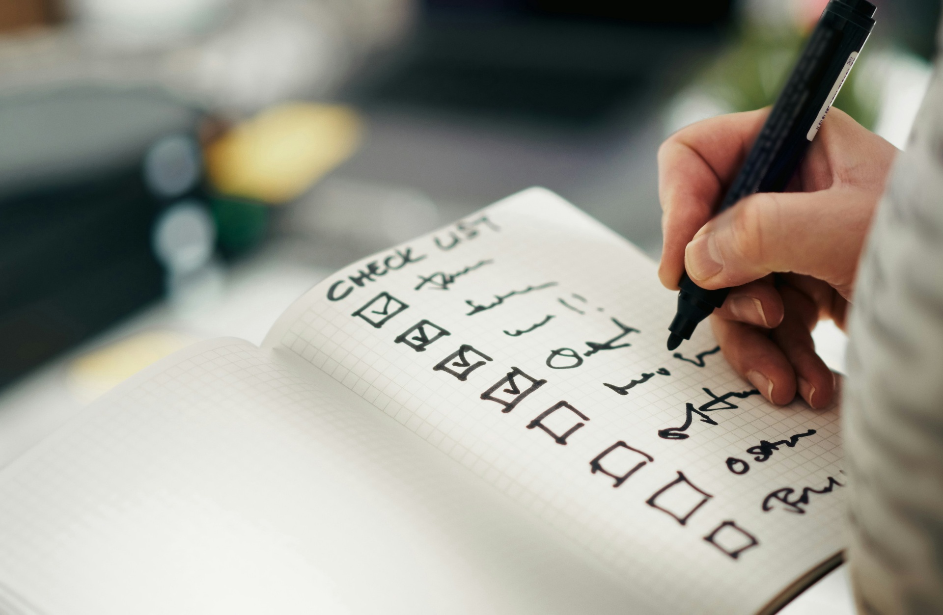 Person checking items off a handwritten go-live checklist in a graph-paper notebook with a black marker.